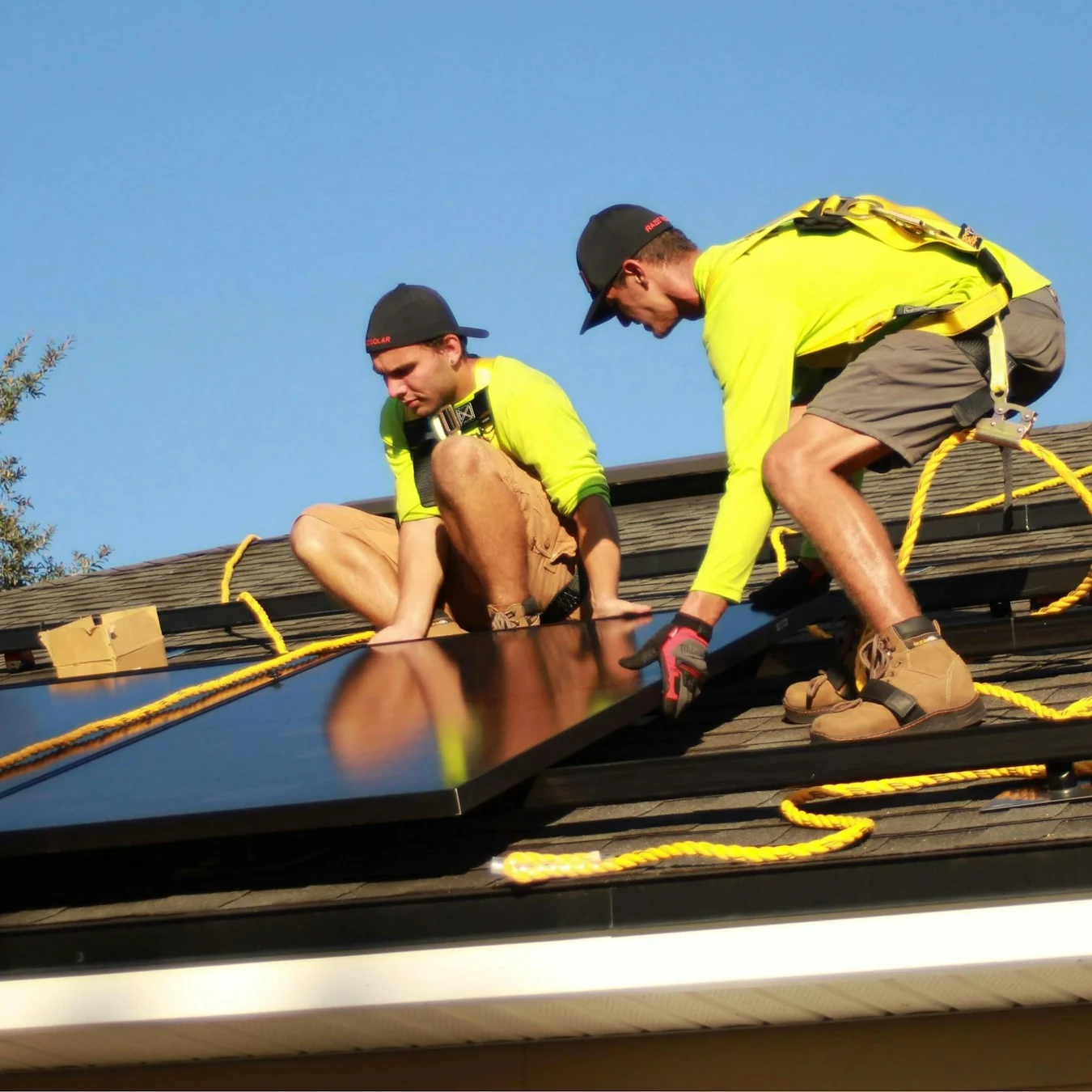 Two installers in high-visibility shirts fitting solar panels on a roof under a clear sky