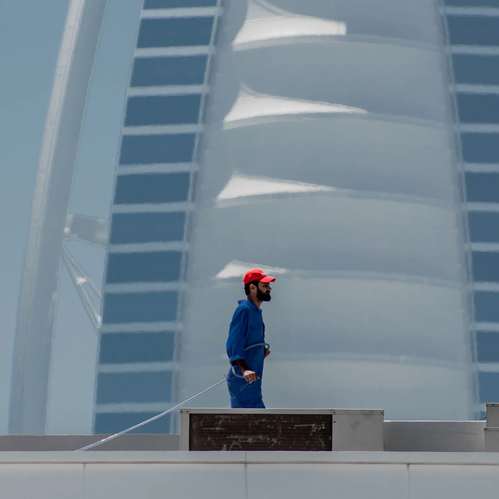 A maintenance worker on a Dubai rooftop with the Burj Al Arab behind him